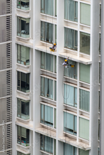 Two men at the exterior of a high-rise building. One working at height cleaning window and the other one sleeping on the job