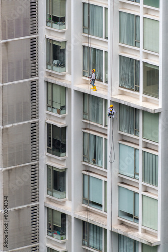 Two men working at height in a high-rise condo in Asia wearing safety harness and wearing helmets