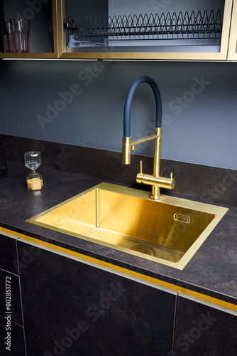 Luxurious interior square golden brass sink and faucet double tap mixer in contemporary modern design with stone marble stoneware countertop black and gold kitchen with sandwatch and glass pot