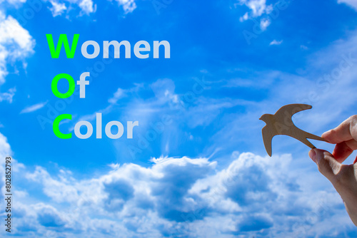 WOC women of color symbol. Concept words WOC women of color on beautiful blue sky clouds background. Wooden bird. Businessman hand. Business WOC women of color social issues concept. Copy space.