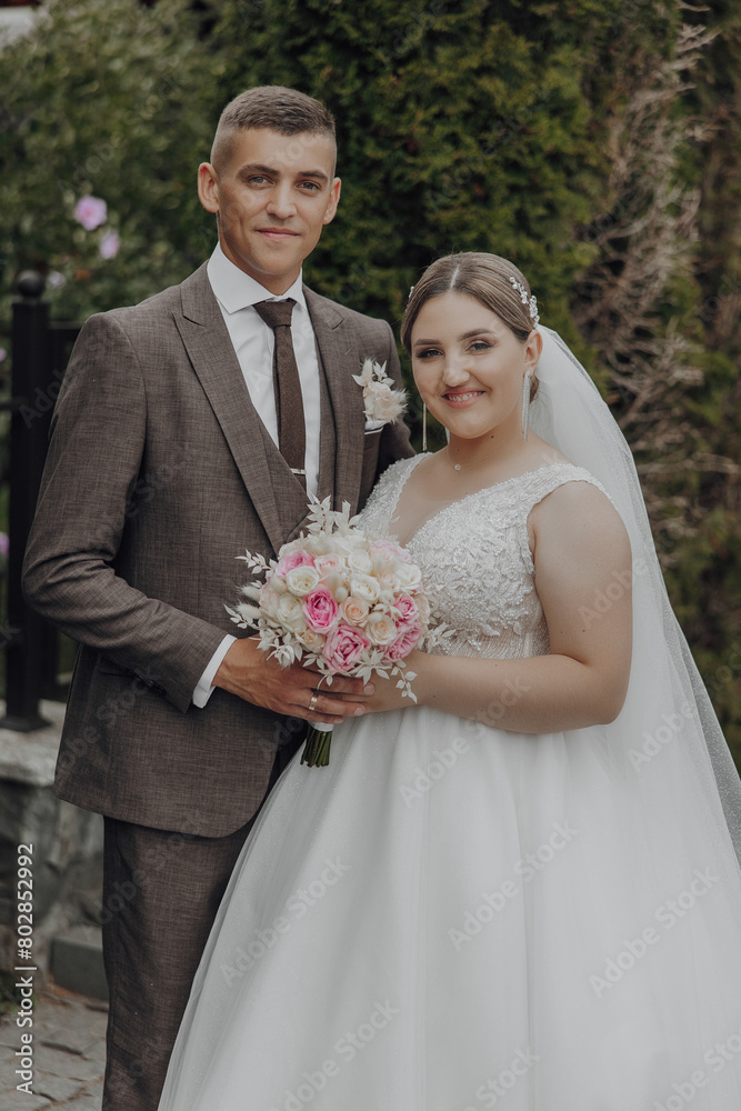 A bride and groom are posing for a picture. The bride is wearing a white dress and the groom is wearing a suit. They are holding a bouquet and a bouquet of flowers A bride and groom are posing for a picture. The bride is wearing a white dress and the groom is wearing a suit. They are holding a bouquet and a bouquet of flowers
