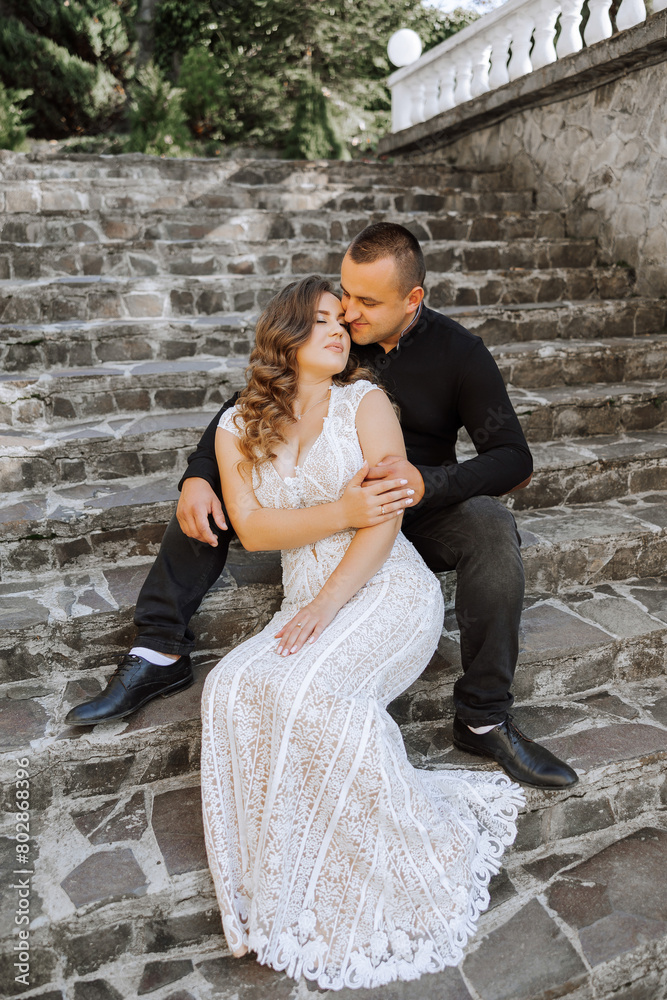 A man and woman are sitting on a set of stairs, the woman is wearing a white dress