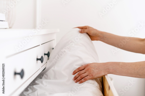 Woman folds white blanket to the chest of drawers