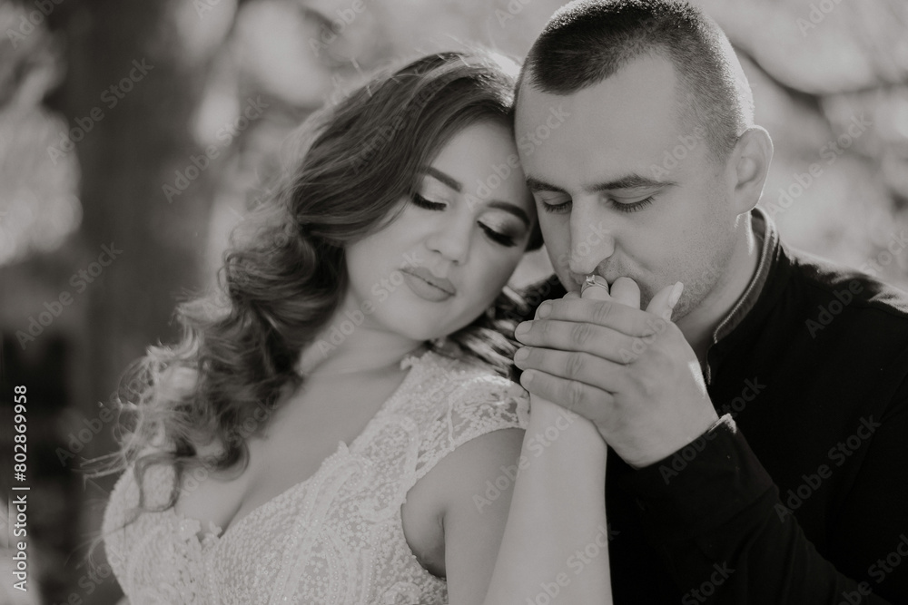 Fototapeta premium A man and a woman are embracing each other. The man is wearing a black shirt and the woman is wearing a white dress. Scene is romantic and intimate