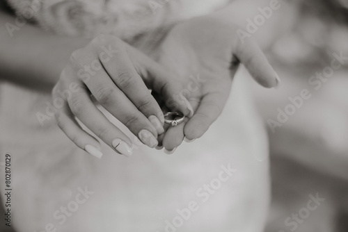 A woman is holding a ring in her hand. The ring is silver and has a diamond on it. The woman is wearing a white dress and she is in a wedding or formal setting. Concept of elegance and sophistication