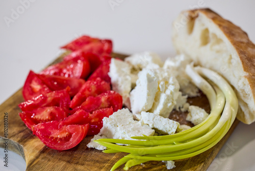 Cheese, tomatoes, green onions and bread on a wooden plate.