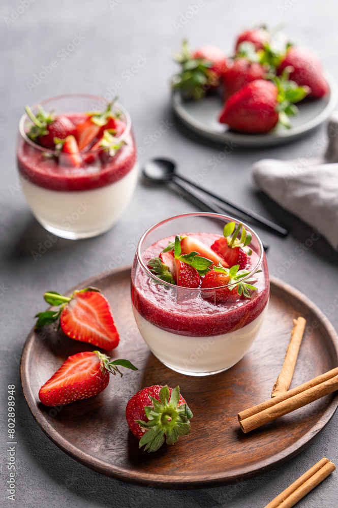 Strawberry and cream panna cotta in glasses with fresh berries on a wooden plate on a light background with cinammon.
