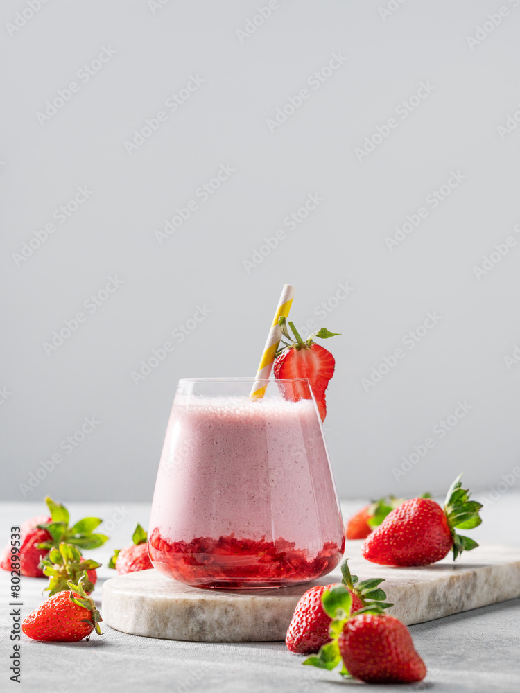 A glass of strawberry milkshake or smoothie with strawberries on a marble board with fresh berries. A glass of strawberry milkshake or smoothie with strawberries on a marble board with fresh berries.
