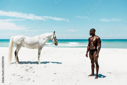 black man on the beach in black swimwear near white horse with blue sky background