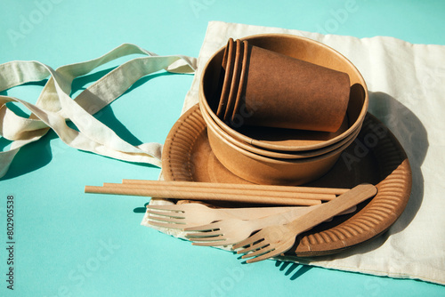 A paper utensils, plates and wooden cutlery on a textile bag on a blue background. Eco friendly pattern, zero waste concept. Top view