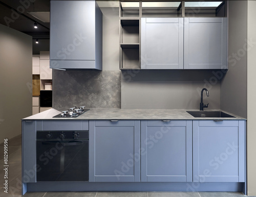 Blue gray contemporary kitchen linearlayout with hood, two burners gas cooker hob oven and built in dishwasher machine, square black sink and tap. Compact high pressure laminate HPL countertop