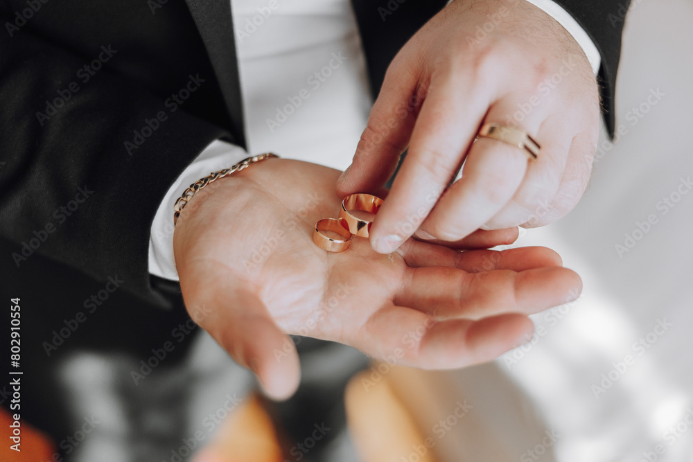 Fototapeta premium A man is holding three gold rings in his hand. The rings are of different sizes and are placed in a row. The man is admiring the rings or possibly preparing to give them to someone