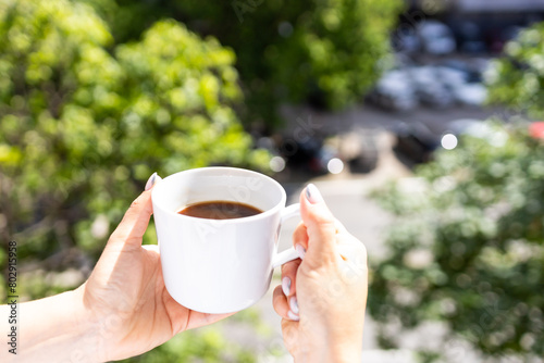A young woman enjoys a cup of freshly brewed coffee on the balcony of her apartment.