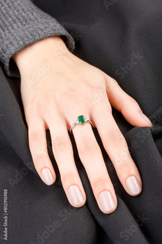 Beautiful female hand with gold ring with diamonds and emerald on gray background