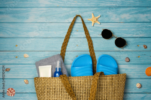 Beach bag with things on a blue wooden background. Top view, copy space