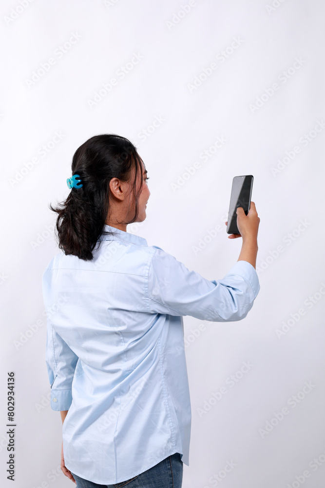 Back view of Adult Asian woman wearing bright blue shirt holding and looking to mobile phone screen. Isolated on white Back view of Adult Asian woman wearing bright blue shirt holding and looking to mobile phone screen. Isolated on white