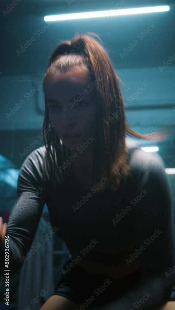 Athletic woman trains with battle ropes in dim boxing gym with LED lighting. Professional female boxer does cardio or endurance exercises before fighting competition. Vertical shot Athletic woman trains with battle ropes in dim boxing gym with LED lighting. Professional female boxer does cardio or endurance exercises before fighting competition. Vertical shot