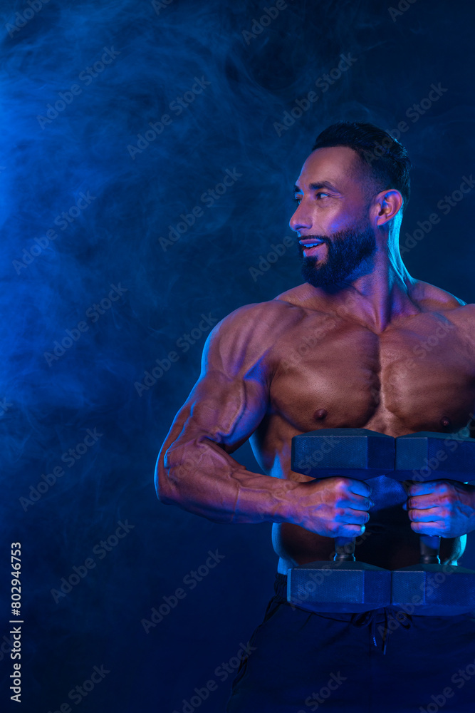 Sporty fit man athlete with dumbbells make fitness exercises on neon background. Download cover for music collection for fitness classes. Sports recreation.