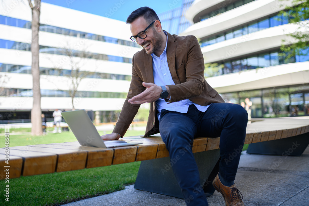 Positive entrepreneur discussing over video call on laptop while sitting on bench against buildings Positive entrepreneur discussing over video call on laptop while sitting on bench against buildings
