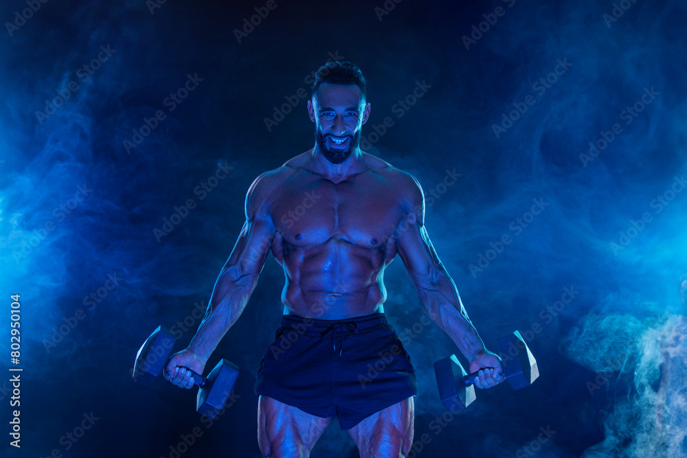 Sporty fit man athlete with dumbbells make fitness exercises on blue neon background. Download cover for music collection for fitness classes. Sports recreation. Sporty fit man athlete with dumbbells make fitness exercises on blue neon background. Download cover for music collection for fitness classes. Sports recreation.