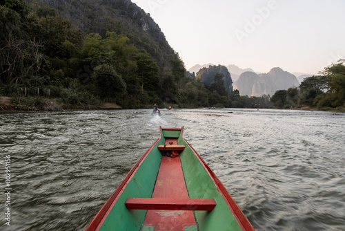wooden boat going down the river with mountains in Vang Vieng, the adventure capital of Laos