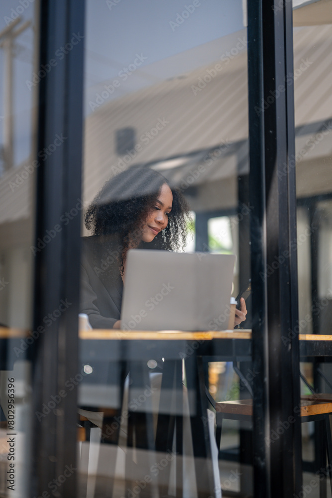 A woman is looking out a window at a laptop. She is waving to someone on the other side of the window