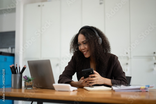 A woman is sitting at a desk with a laptop and a cell phone. She is smiling and she is enjoying herself