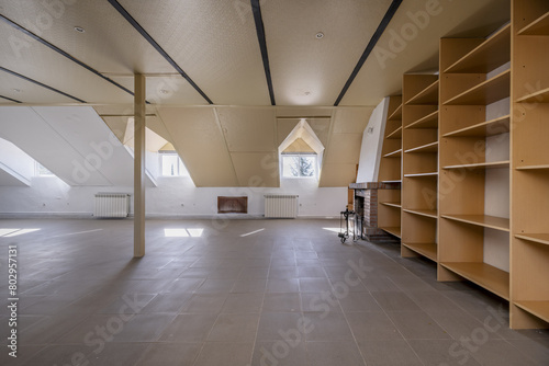 Large attic of a house with a wall covered with wooden shelves with skylights with windows photo