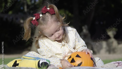 Close up of adorable little girl sitting on the blanket and playing with the halloween pumpkin in the city park photo