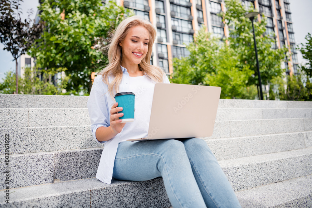 Photo of young smiling woman remote working sitting using laptop for research new trend in marketing industry take coffee to go outdoors Photo of young smiling woman remote working sitting using laptop for research new trend in marketing industry take coffee to go outdoors