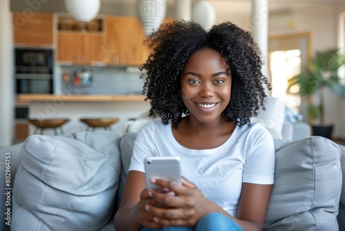 Excited young african-american woman smiling while using smartphone on comfortable sofa at home