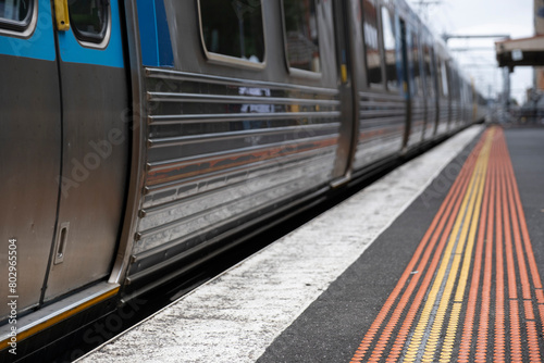 Railway station platform with yellow and red safety dots, and a departing PTV metro train in Melbourne, Australia. Focus on the dots in front and the doors at the left