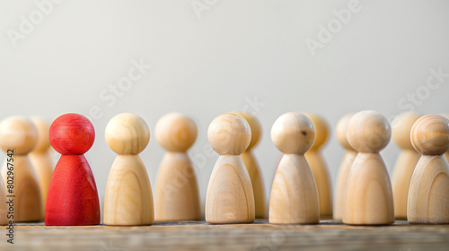 Row of wooden figurines with one distinct red figurine standing out, symbolizing leadership, individuality, and teamwork in a minimalist setting. Concept of diversity, uniqueness, and team dynamics.