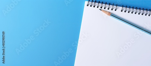 A blank white paper with a pencil placed on top against a blue background offering space for adding text or images. with copy space image. Place for adding text or design