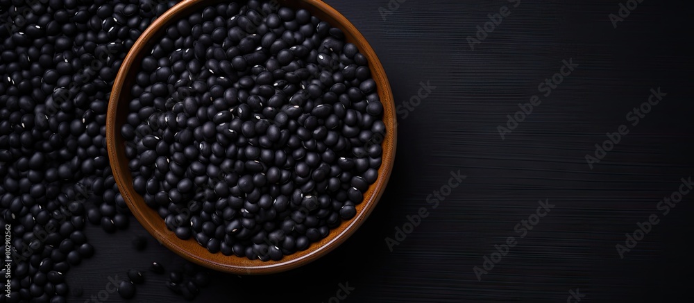 A black bowl filled with black beans is seen from above on a black background in this copy space image A black bowl filled with black beans is seen from above on a black background in this copy space image