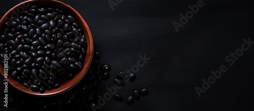 A black bowl filled with black beans is seen from above on a black background in this copy space image photo