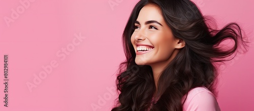 A cheerful brunette girl happily chats on the phone and smiles while standing against a pink studio backdrop with her gaze fixed on a copy space image This image conveys the concept of promotions sal photo
