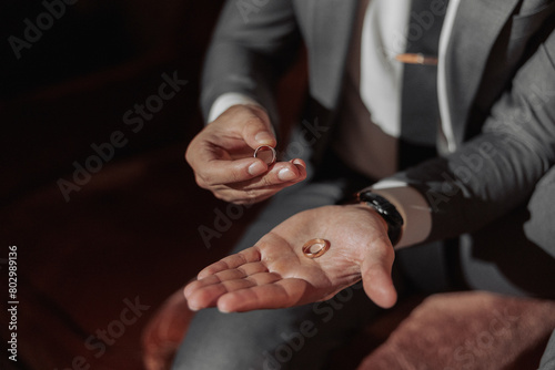 A man is holding two rings in his hands, one of which is a wedding ring. Concept of love and commitment, as the man is likely about to propose to his partner. The setting is intimate and romantic
