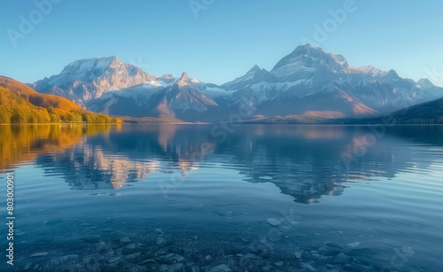Mountain Reflected in Lake. The clear lake water reflects the majestic mountains in the distance, creating an endless and peaceful scene of nature. The golden light shines on part of the mountain © RumRaisinStock