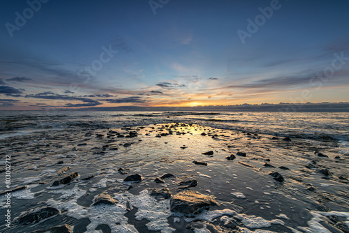 The stones of the pier emerge as the North Sea recedes during a colorful sunset. The peak of the tide has passed, gradually revealing the pier. The water of the North Sea recedes.