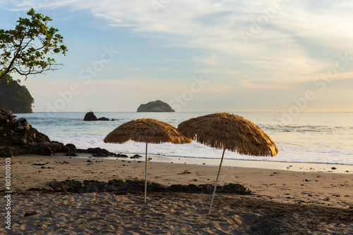 Two straw parasols planted on deserted beach seen at dusk, with small island in the Pacific Ocean in the background, Manuel Antonio, Puntarenas province, Costa Rica
