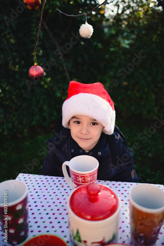Cute boy with red christmas hat with tea cup in nature background