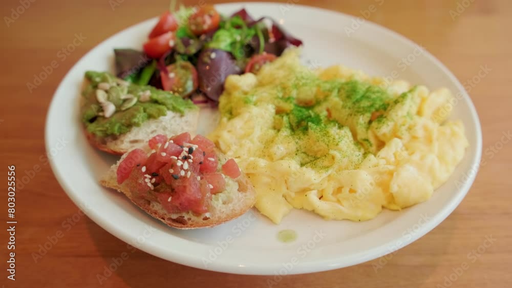 A nutritious brunch serving with fluffy scrambled eggs, a vibrant mixed salad, avocado toast, and seeds.