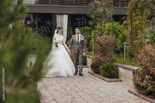 A bride and groom are walking down a path in a garden. The bride is wearing a white dress and the groom is wearing a gray suit. They are holding hands and appear to be happy