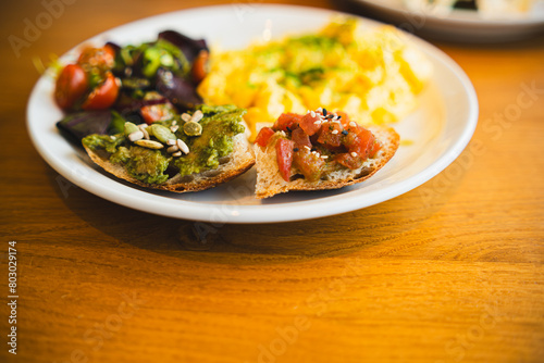 A nutritious brunch serving with fluffy scrambled eggs, a vibrant mixed salad, avocado toast, and seeds.