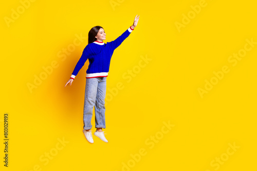 Full length photo of pretty teen girl jumping hanging wear trendy knitwear blue outfit isolated on yellow color background