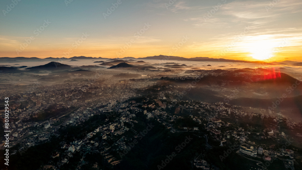 An aerial view of Da Lat city nestled among green hills, with a lake in the foreground.