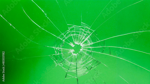 A hole with cracks in the glass. Broken window on a green background photo