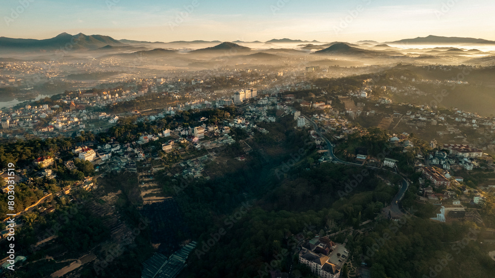 Obraz premium An aerial view of Da Lat city nestled among green hills, with a lake in the foreground.