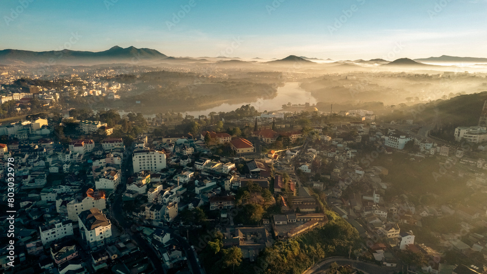 Obraz premium an aerial view of a city at sunset. The sky is ablaze with orange, pink, and purple hues, casting a warm glow on the city below. Buildings of various shapes and sizes are visible, including skyscrape